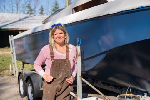 Mature woman smiling at camera while leaning against a boat in her yard.