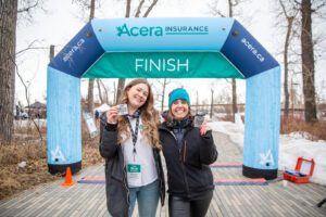 Two participants pose with medals by the Acera Insurance finish line.